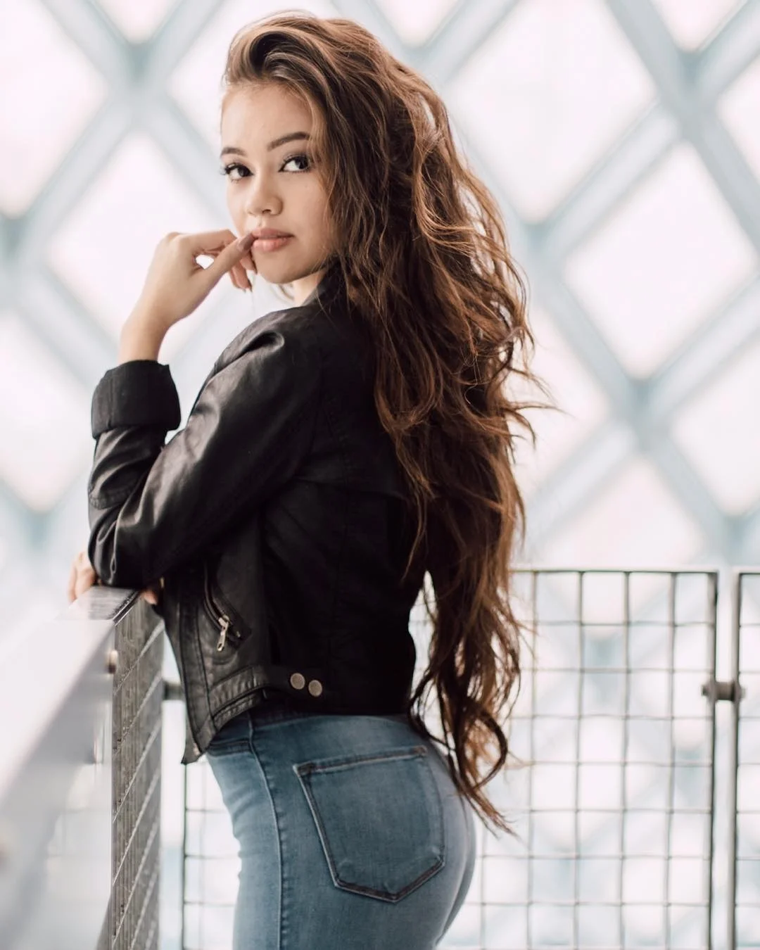 Hình ảnh gái xinh Việt Nam xinh đẹp với mái tóc dài gợn sóng, mặc áo khoác da đen và quần jeans, tạo dáng tự tin ngoài trời
